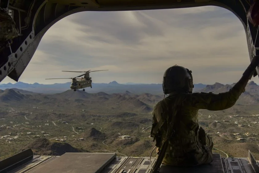 View from inside a military transport helicopter looking out at a Chinook in flight, representing CMMC Level 3 compliance for advanced aerospace programs.