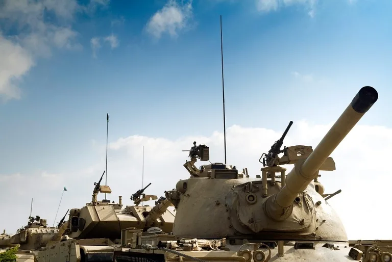 A line of military tanks under a blue sky, representing the defense industrial base sectors served by C3PAO CMMC assessments.