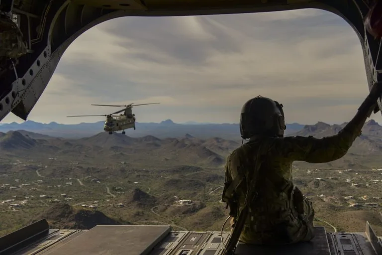 View from inside a military transport helicopter looking out at a Chinook in flight, representing CMMC Level 3 compliance for advanced aerospace programs.