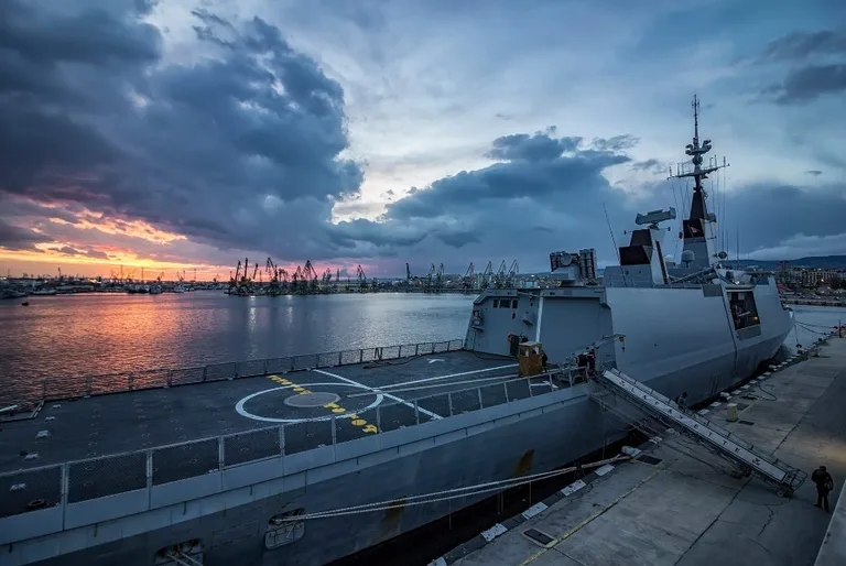 A military frigate docked at sunset, representing the maritime defense contractors served by CMMC mock assessments.